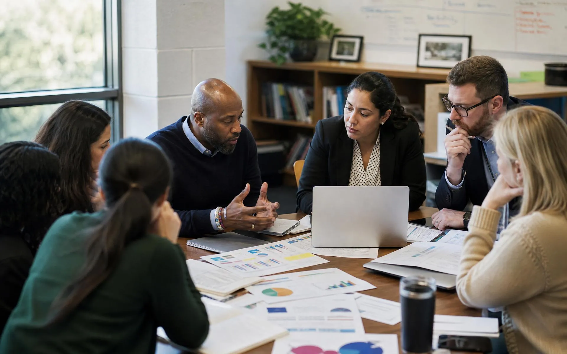 Educators gathered around a table reviewing student work and assessment data together